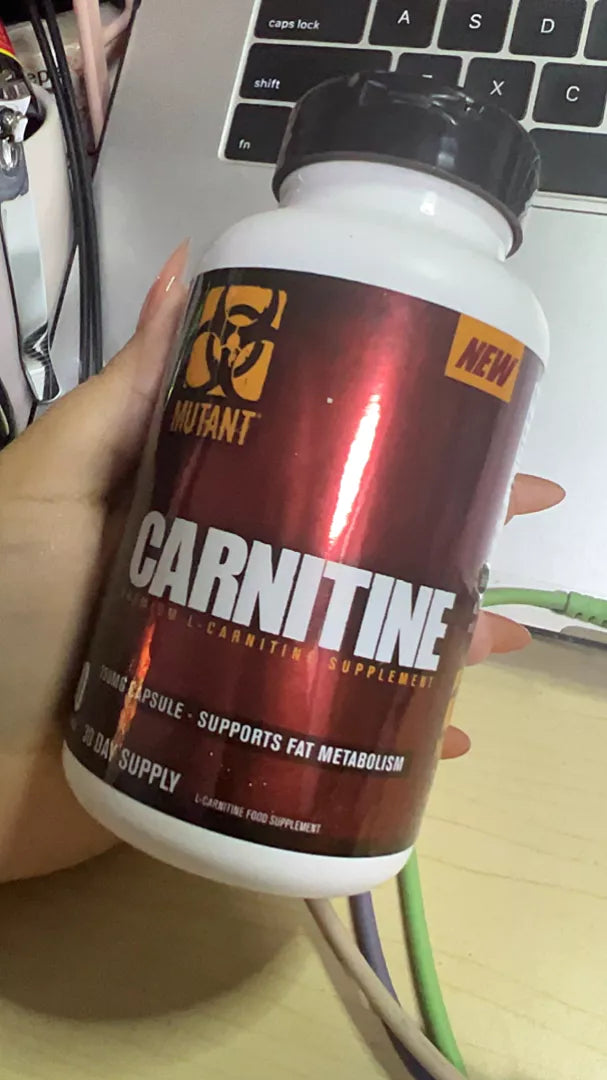 Mutant L-Carnitine bottle held in hand beside a laptop